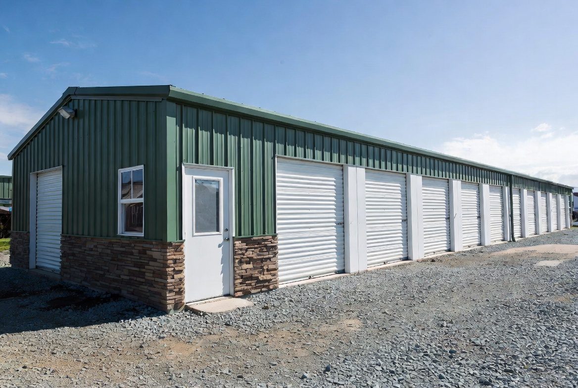 Green mini storage building with stone accent and row of white roll-up doors